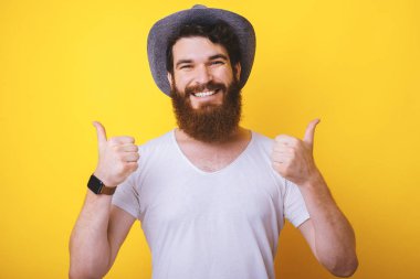 Neşeli genç sakallı hipster başparmak gösteren kameraya gülümseyen.