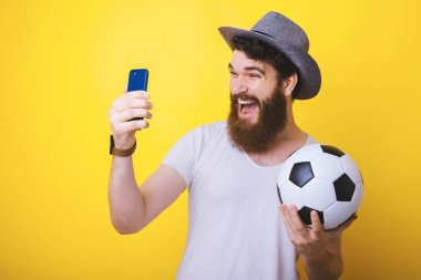 Genç sakallı adam bağırıyor ve takımının kazandığı mutlulukgülümsüyor. Futbol ve futbol topu. Telefonunu izleyen adam.