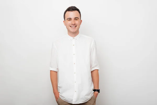 Retrato de un joven sonriente que sostiene sus manos en los bolsillos de sus pantalones sobre fondo blanco . —  Fotos de Stock