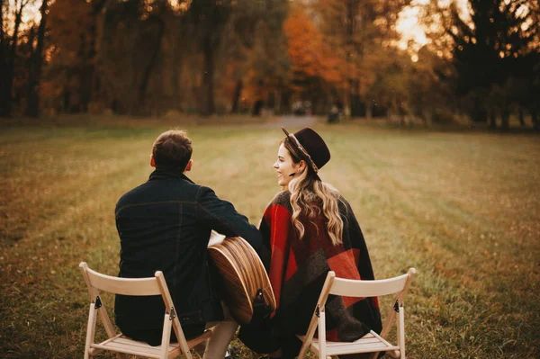 Mann und Frau sitzen bei Sonnenuntergang im Park und spielen an der Gitarre, romantisches Paarkonzept — Stockfoto