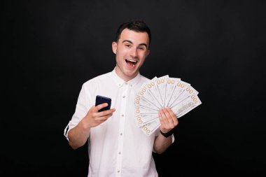 Beyaz gömlek genç neşeli adam siyah arka plan üzerinde bir telefon ve bazı faturaları tutar