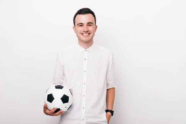 Jovem alegre em camisa branca segurando uma bola de futebol e olhando para a câmera feliz no fundo branco — Fotografia de Stock