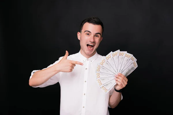 Junger Mann im weißen Hemd zeigt die Scheine aus seiner Hand auf schwarzem Hintergrund — Stockfoto