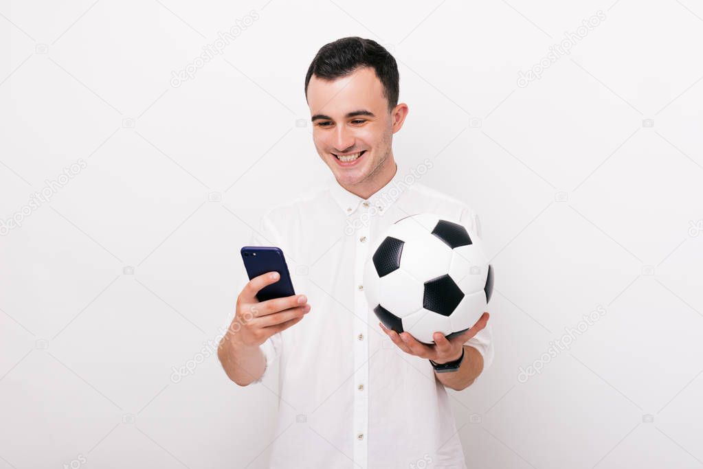 Photo of young happy man in casual holding smartphone and soccer ball