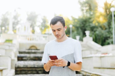 Düşünceli bir genç adam telefona bakıyor ve parkta müzik dinliyor..