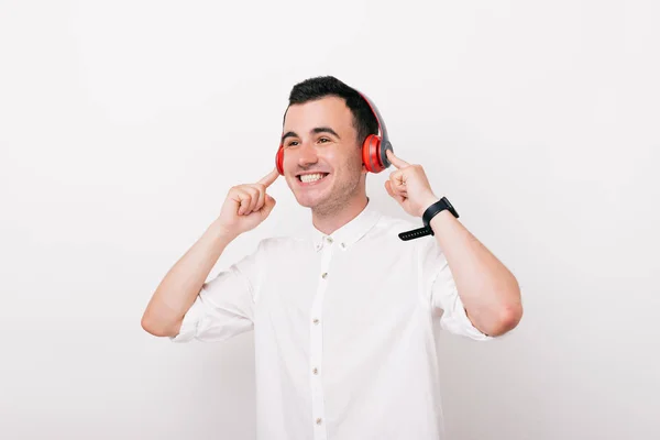 Ein glücklicher junger Mann hört der Musik zu und lächelt im Studio auf weißem Hintergrund. — Stockfoto