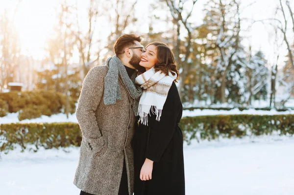 Vidám fiatal pár, ahol az ember megcsókolja a lányt arcán a parkban. — Stock Fotó