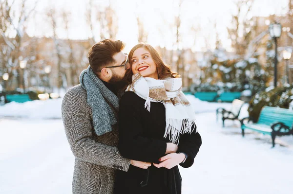 Una feliz pareja abrazada, donde el hombre da un beso en la mejilla a la mujer en el parque en invierno . — Foto de Stock