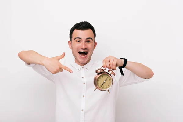 Fröhlicher junger Mann zeigt eine Uhr im Atelier auf weißem Hintergrund. — Stockfoto
