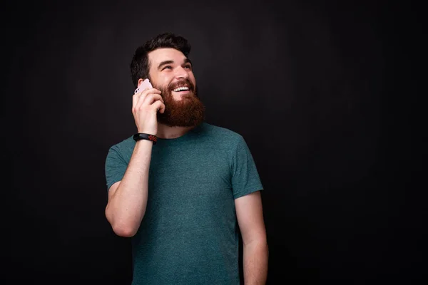 Hello, how are you? Young bearded man talking on the phone on black background.