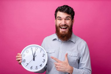 It's satış zamanı! Genç sakallı adam beyaz bir saat tutuyor ve pembe arka plan üzerinde işaret ediyor.