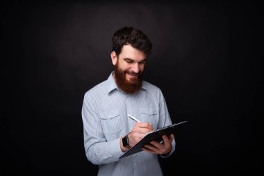 Genç sakallı adam siyah arka plan üzerinde bir el tahtası üzerinde notlar alıyor.