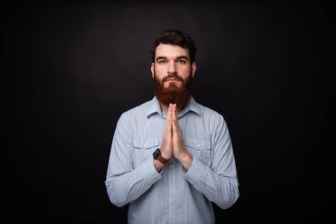 Let's dua! Genç sakallı adam siyah arka planda dua poz el ele tutuşuyor.
