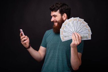 Telefonunda bahse bahse yeni çıkan genç sakallı adam elinde bir sürü para tutuyor..
