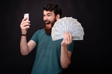 Ben zenginim! Ben kazandım! Genç sakallı adam telefonuna bakarak ve elinde bir demet para tutarak şaşırttı