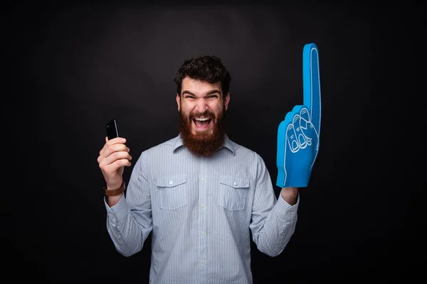 I won! Go team! Great fan, bearded man holding his phone and a fan glove nr 1 on black background.