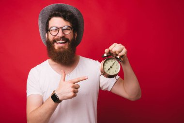  It's zaman !!! Mutlu yüzlü gözlükyakışıklı sakallı adam, bir vintage saat tutan, kırmızı arka plan üzerinde