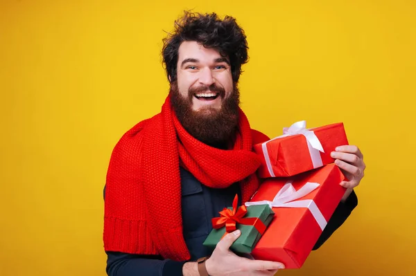 Όμορφος άνθρωπος με γένια με κόκκινο κασκόλ, κρατώντας κουτιά δώρων, ιδέα πώλησης, απολαμβάνοντας δώρα, απομονωμένο κίτρινο φόντο — Φωτογραφία Αρχείου