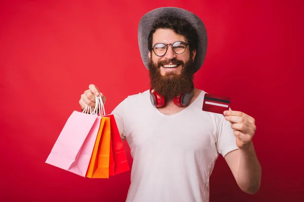 It's shopping time ! Photo of stylish bearded guy shopping with new credit card, over red background