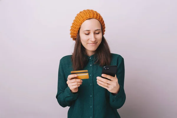 Retrato de mulher jovem, segurando um telefone celular e um cartão de crédito, compras on-line sobre fundo isolado — Fotografia de Stock