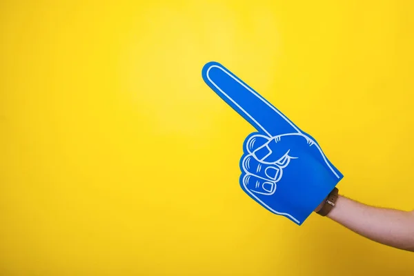 Photo of a handsome arm,  wearing a big blue fan glove, over isolated yellow background — Stock Photo, Image