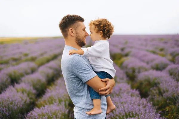 Photo of young father holding and hugging his little curly boy, having fun together, and posing in a lavender field — Stock Photo, Image