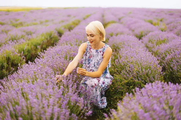 Foto de una mujer rubia, recogiendo un ramo de flores, en un campo de lavanda — Foto de Stock