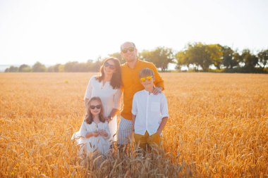 Bir buğday tarlasında vakit geçiren, poz veren ve kameraya bakan bir ailenin fotoğrafı