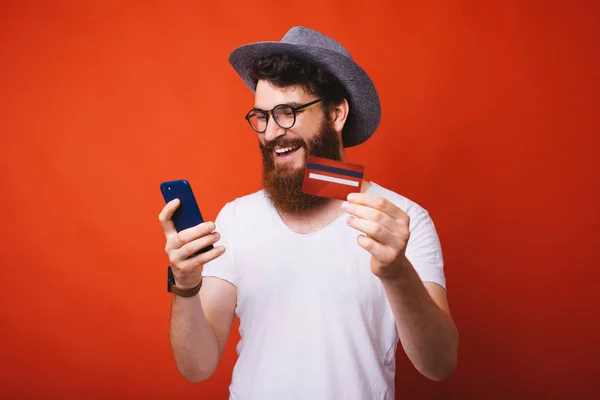 英俊的胡子男子的照片 使用手机在线购物 并在相机显示信用卡 — 图库照片