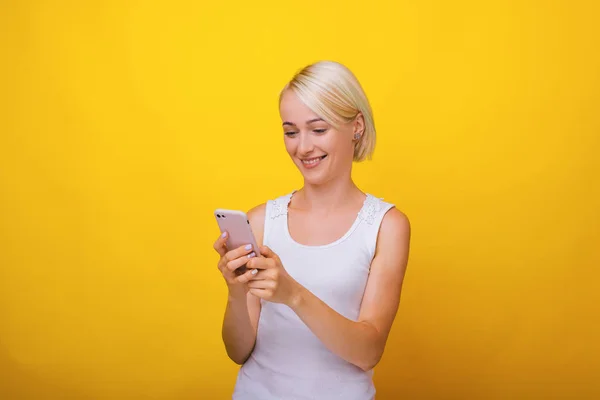 Retrato de mulher loira sorridente, usando telefone celular sobre amarelo — Fotografia de Stock