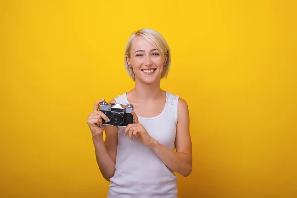 A young blonde woman, holding a vintage camera and trying to tak — Stock Photo, Image