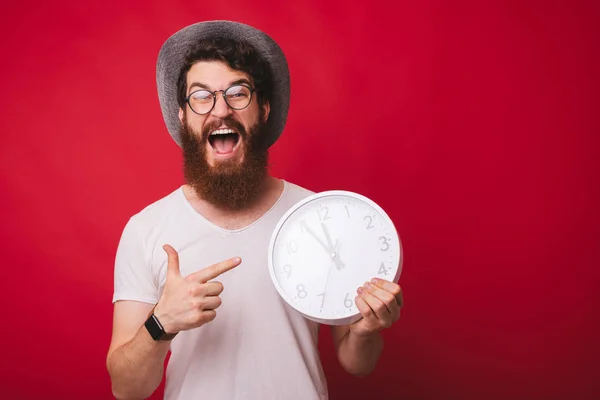 Photo of excited bearded guy, pointing at clok,standing over red — Stock Photo, Image