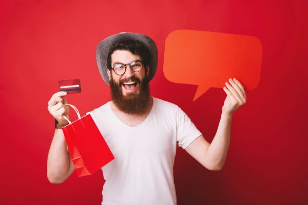Jovem feliz com barba segurando bolha de discurso vermelho e crédito — Fotografia de Stock