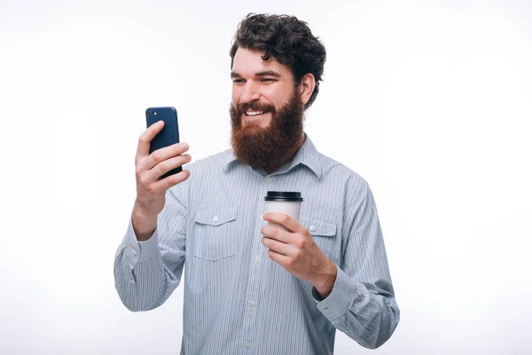 Foto del hombre excitado usando su teléfono inteligente y sosteniendo la taza de cof —  Fotos de Stock