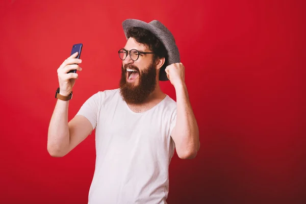 Portrait of amazed bearded hipster man looking at phone and cele — Stock Photo, Image