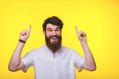 Neşeli sakallı adam sarı duvarda kopyalama alanı iki eliyle işaret.
