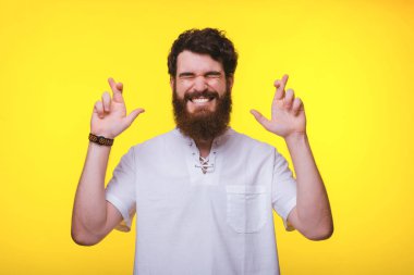 Genç sakallı adam sarı arka plan yakınında çapraz parmakları ile duruyor.