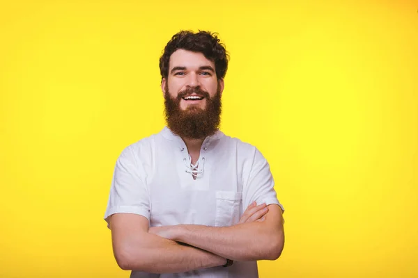 Homem barbudo está sorrindo para a câmera com os braços cruzados no fundo amarelo nd . — Fotografia de Stock