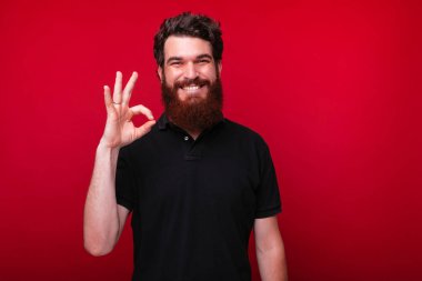 Gülümseyen sakallı adam kırmızı duvarda Ok jest gösteriyor