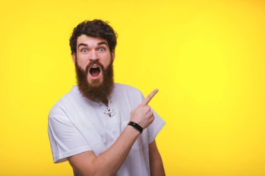 Neşeli genç sakallı adam gülümseyerek ve sarı arka plan yakınındaki copyspace uzağa işaret.