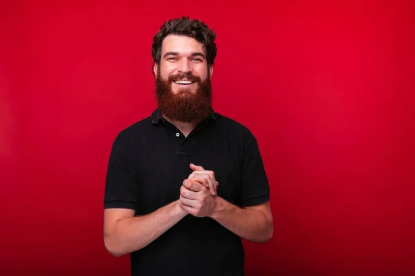 Retrato de hombre barbudo alegre de pie sobre fondo rojo en el estudio y mirando a la cámara —  Fotos de Stock