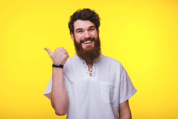 黄色の背景に親指を上げるカジュアルで陽気な若いひげの男. — ストック写真