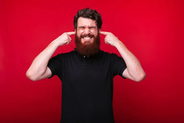 Egy szakállas fiatalember, amely a fülét vörös alapon fedi — Stock Fotó