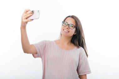 Mutlu kızın beyaz arka plan üzerinden akıllı telefonla gülümseyip selfie çektiği fotoğraf