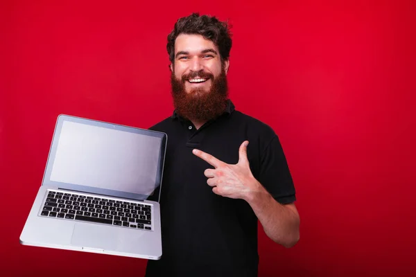 Foto eines gutaussehenden bärtigen Kerls, der auf den stehenden Laptop zeigt — Stockfoto