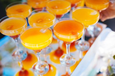 Ayna tepsisinde kokteyl bardaklarında portakal içecekleri. Açık bar.