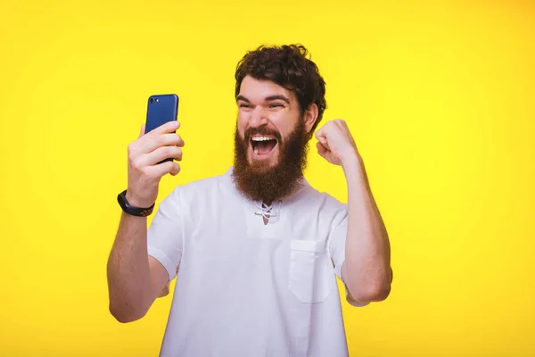 Feliz barbudo ganador gritando y mirando su teléfono sobre fondo amarillo . —  Fotos de Stock