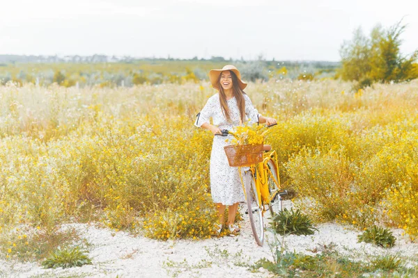 Romantyczna młoda dama śmieje się podczas noszenia jej rocznika żółty rower na kwitnące pole. — Zdjęcie stockowe