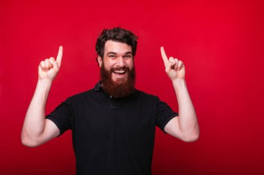 Şuna bak! Adam gülümseyen ve kırmızı arka plan üzerinde iki eliyle yukarı işaret.