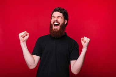 Ben kazandım! Genç sakallı adam kırmızı arka plan üzerinde çığlık kazanan jest yapma.